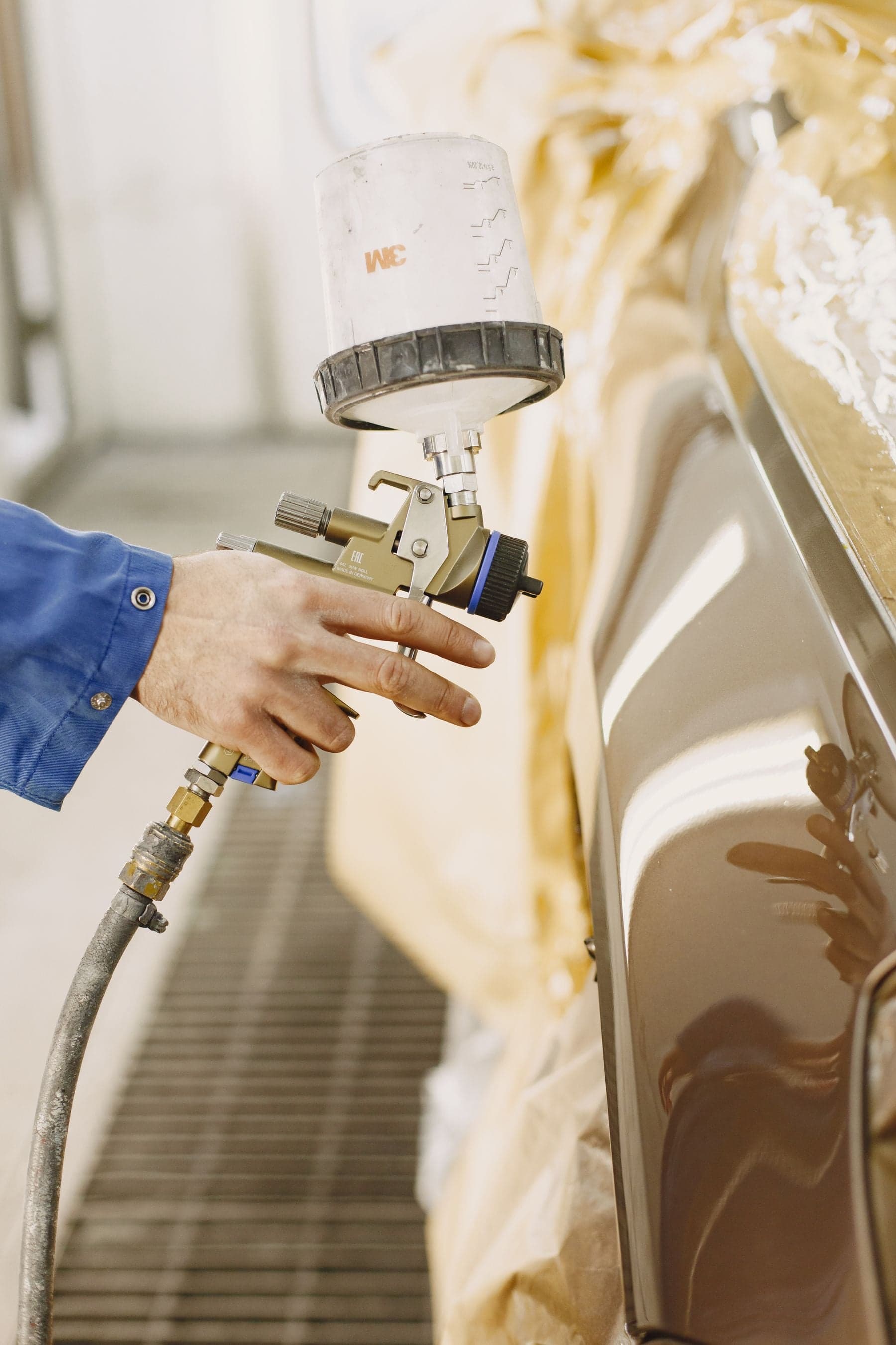 A technician applying paint to a masked vehicle body panel with a spray gun